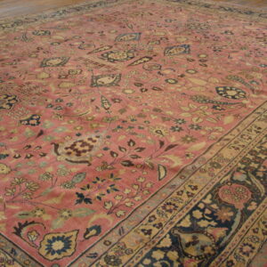 Pink low-pile rug with an all-over traditional floral pattern and contrasting navy and tan borders on wood flooring.