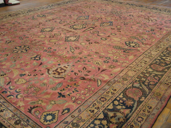 Pink low-pile rug with an all-over traditional floral pattern and contrasting navy and tan borders on wood flooring.