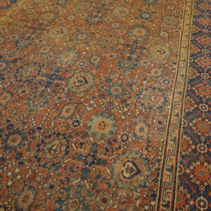 Intricate rust and navy rug featuring an all-over floral pattern and a wide decorative border on wood floors.