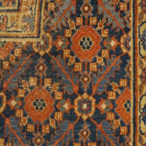 Close up of a rug with deep blue, rust, light blue, and tan geometric patterns next to wood flooring.