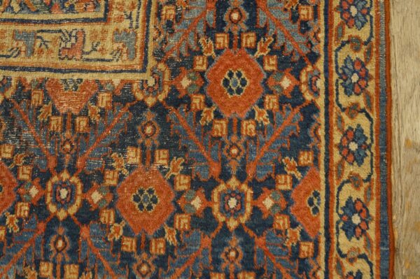Close up of a rug with deep blue, rust, light blue, and tan geometric patterns next to wood flooring.