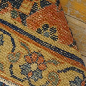 Detail of a low-pile rug showing navy, orange, and gold ornate motifs against yellow distressed wood.