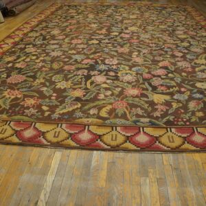 Large brown rug with colorful floral motifs and a bold yellow and red scalloped border on hardwood flooring.