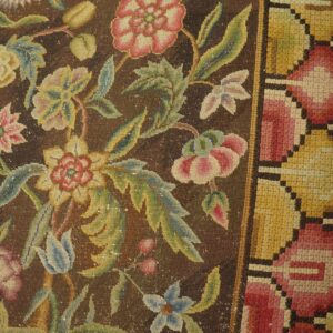 Dark brown low-pile rug featuring pink, yellow, and green floral designs next to light wood flooring.