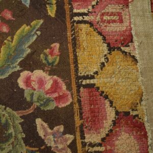 Textured rug detail featuring pink and green floral patterns next to yellow loops, partially covered by a canvas strip.