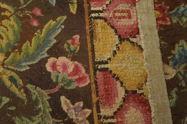 Textured rug detail featuring pink and green floral patterns next to yellow loops, partially covered by a canvas strip.