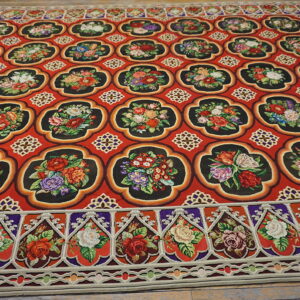 Bright red rug with high-contrast black quatrefoil motifs filled with multicolored floral patterns on wood flooring.