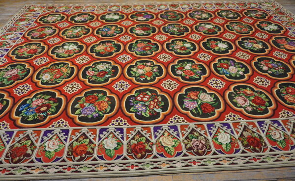 Bright red rug with high-contrast black quatrefoil motifs filled with multicolored floral patterns on wood flooring.