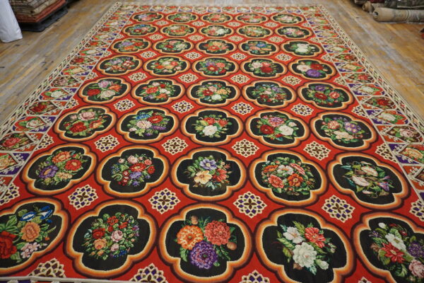 Vibrant red rug with black floral quatrefoils rests on light brown distressed wood planks.