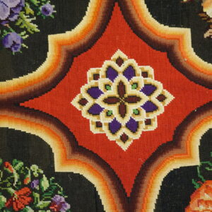 Detailed view of a low-pile rug featuring red geometric medallions, gradient orange borders, and multicolored floral designs on black.