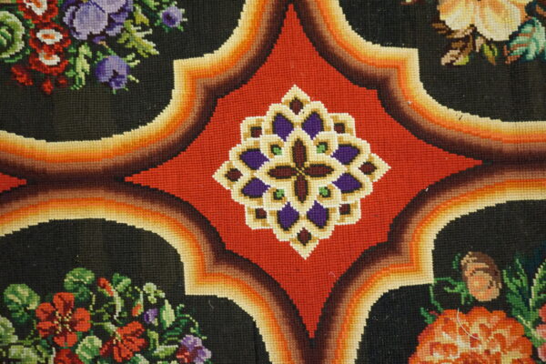 Detailed view of a low-pile rug featuring red geometric medallions, gradient orange borders, and multicolored floral designs on black.