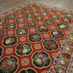 Vibrant red rug with repeating black floral medallions sits on distressed light wood floors.