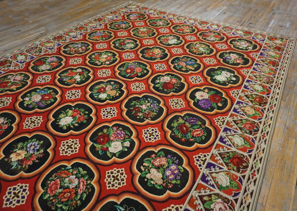 Vibrant red rug with repeating black floral medallions sits on distressed light wood floors.