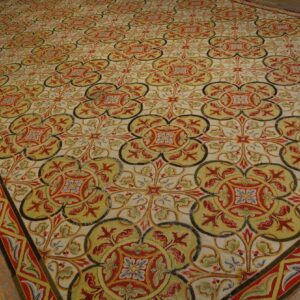 Intricate, large area rug with repeating red, olive, and cream floral medallions on wooden plank floors.