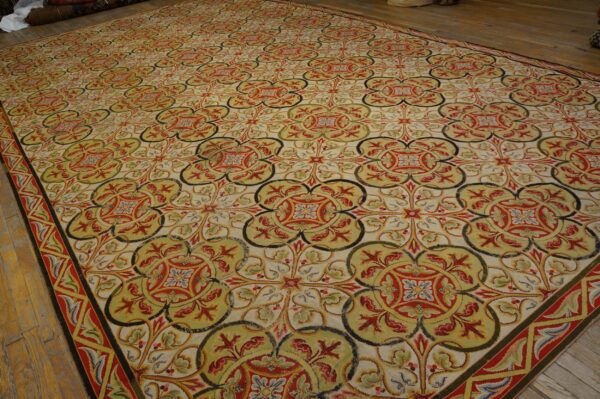 Low-pile rug displaying an intricate quatrefoil pattern in cream, red, olive green, and gold on wood flooring.