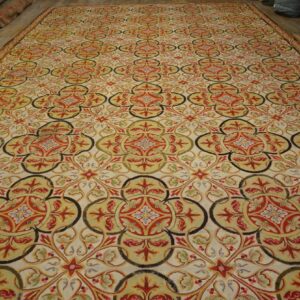 Repeating red, olive, and black scrolling medallion pattern covers a large cream low-pile rug.