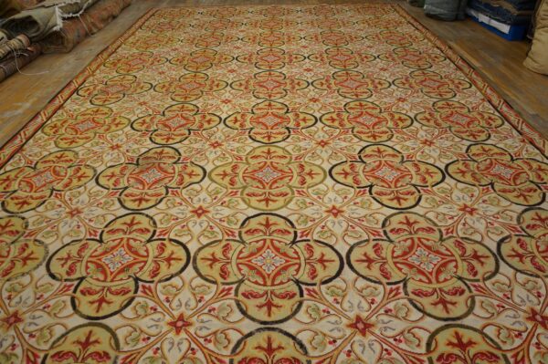 Repeating red, olive, and black scrolling medallion pattern covers a large cream low-pile rug.