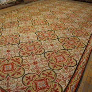 Ornate rug featuring red, gold, and olive green repeating medallions displayed on light brown wood flooring.