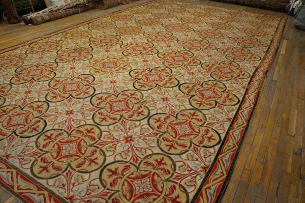 Ornate rug featuring red, gold, and olive green repeating medallions displayed on light brown wood flooring.