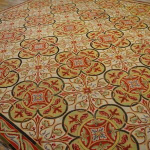 Low-pile rug with interlocking quatrefoil patterns in red, green, yellow, and cream on distressed wood flooring.