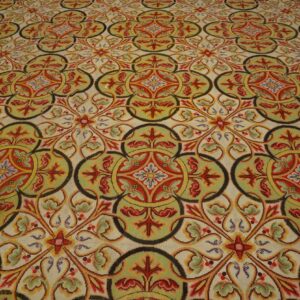 Highly patterned low-pile rug with interlocking red, gold, and olive green medallions on a cream background.