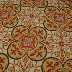 Interlocking scrollwork rug pattern in cream, red, green, and yellow over dark wooden floorboards.