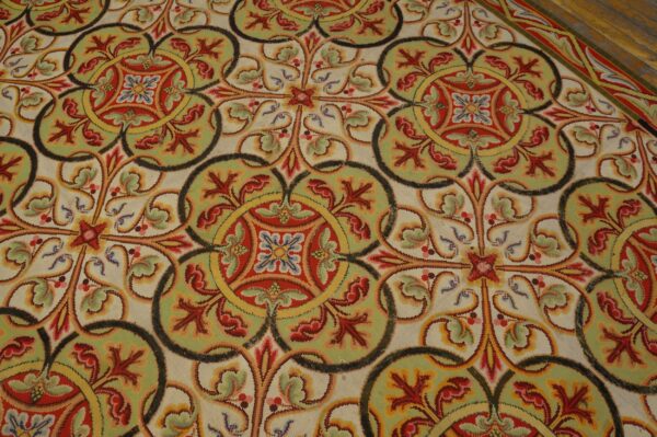 Interlocking scrollwork rug pattern in cream, red, green, and yellow over dark wooden floorboards.