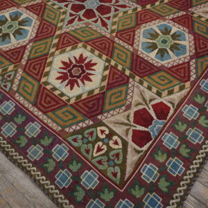 Low-pile rug with geometric and floral medallions in rich colors rests on distressed gray wood flooring.