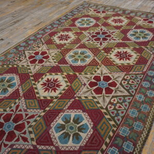 Flat-weave rug with complex red, blue, and gold geometric star patterns resting on worn wooden floorboards.