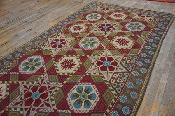 Flat-weave rug with complex red, blue, and gold geometric star patterns resting on worn wooden floorboards.