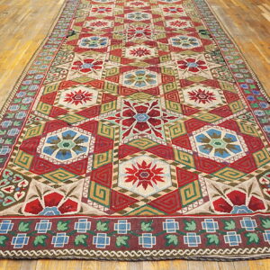 Runner rug with repeating red and blue hexagonal floral designs and complex borders on a wood floor.