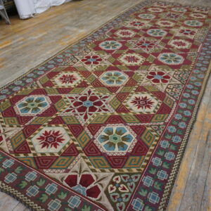 Flatweave rug with repeating medallions in red, blue, green, and tan colors covering a rustic wood floor.