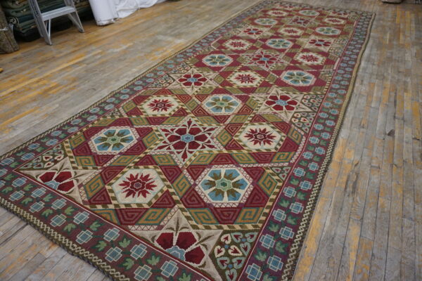 Flatweave rug with repeating medallions in red, blue, green, and tan colors covering a rustic wood floor.