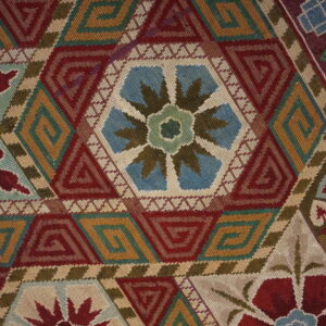 Detailed close-up of a low-pile textile with red, gold, and teal hexagonal geometric patterns and floral motifs.