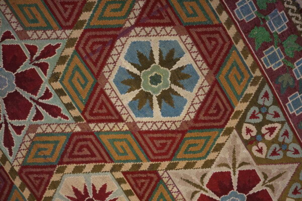 Detailed close-up of a low-pile textile with red, gold, and teal hexagonal geometric patterns and floral motifs.
