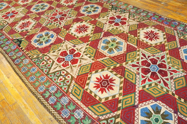 Intricately patterned rug in red, gold, blue, and cream sits angled on wood plank flooring.