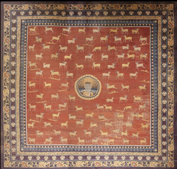 Red square rug featuring scattered tan deer, a central round design, and multi-layered blue and brown borders.