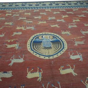 Textured red field rug featuring scattered pale animal figures, a central blue bird medallion, and wide blue borders.