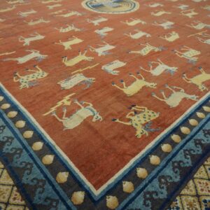 A rust-colored rug featuring repeating yellow and white deer motifs and a complex blue and yellow patterned border.