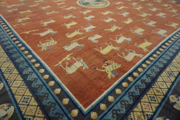A rust-colored rug featuring repeating yellow and white deer motifs and a complex blue and yellow patterned border.