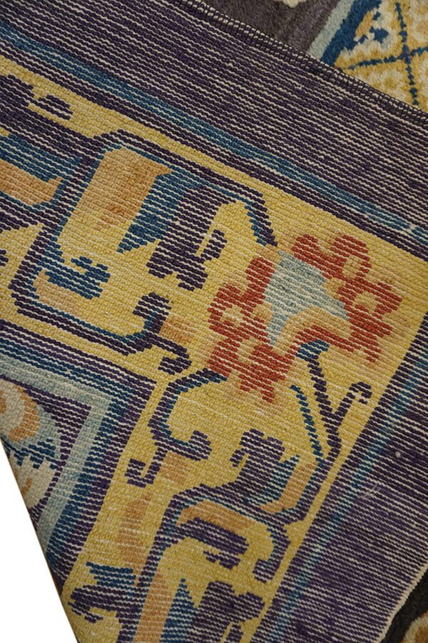 Detail of a woven rug featuring geometric and floral patterns in mustard yellow, purple, blue, and burnt orange.