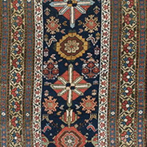 A narrow runner rug featuring a navy blue field with detailed red, beige, and blue geometric medallions and multiple striped borders.