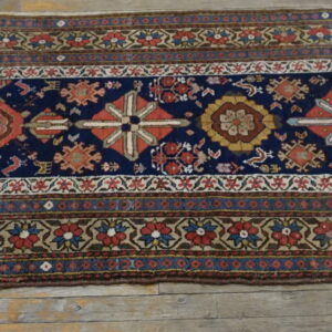 Narrow runner rug with a navy blue field, repeated geometric medallions, and detailed floral borders on wood flooring.