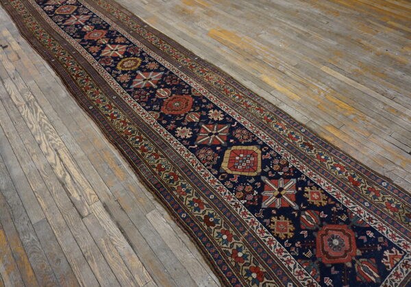 Navy blue runner rug with complex geometric patterns rests on a distressed gray wood floor.