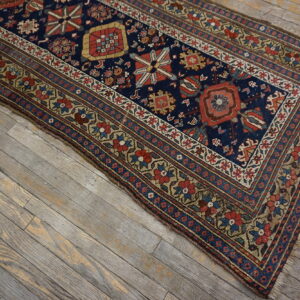 Low-pile runner with navy geometric patterns and floral borders rests on weathered gray wood floor.