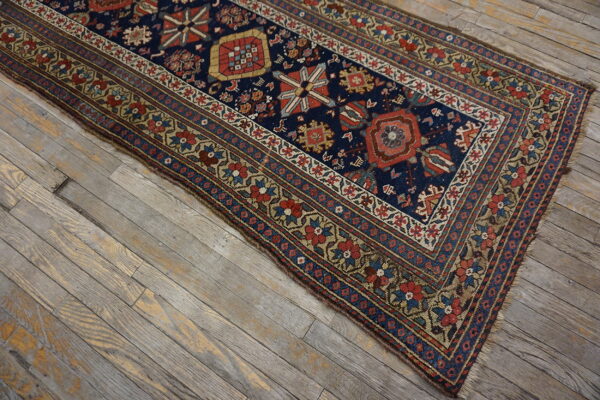 Low-pile runner with navy geometric patterns and floral borders rests on weathered gray wood floor.
