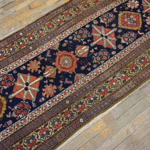 Detailed navy blue, red, and beige runner rug contrasted against light, weathered wooden flooring.