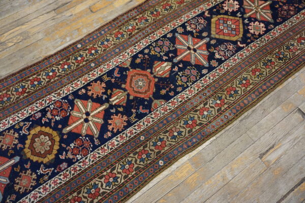 Detailed navy blue, red, and beige runner rug contrasted against light, weathered wooden flooring.