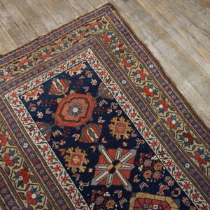 A navy blue traditional rug with red, beige, and blue tribal patterns lies on distressed wood flooring.