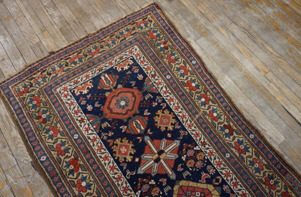 A navy blue traditional rug with red, beige, and blue tribal patterns lies on distressed wood flooring.